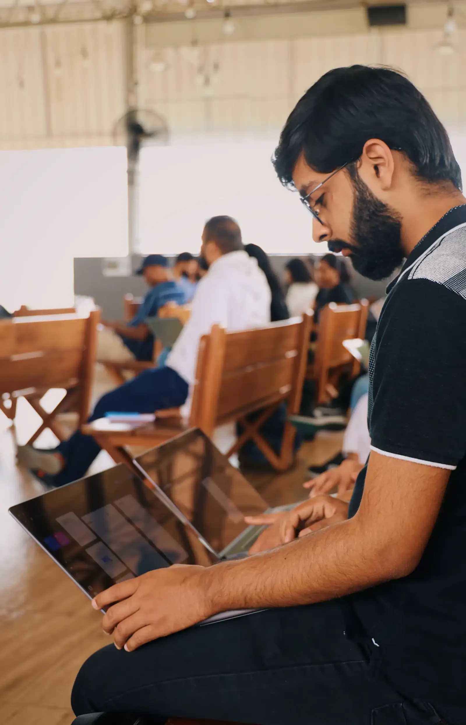 Man working on a laptop in a hall with rows of wooden chairs