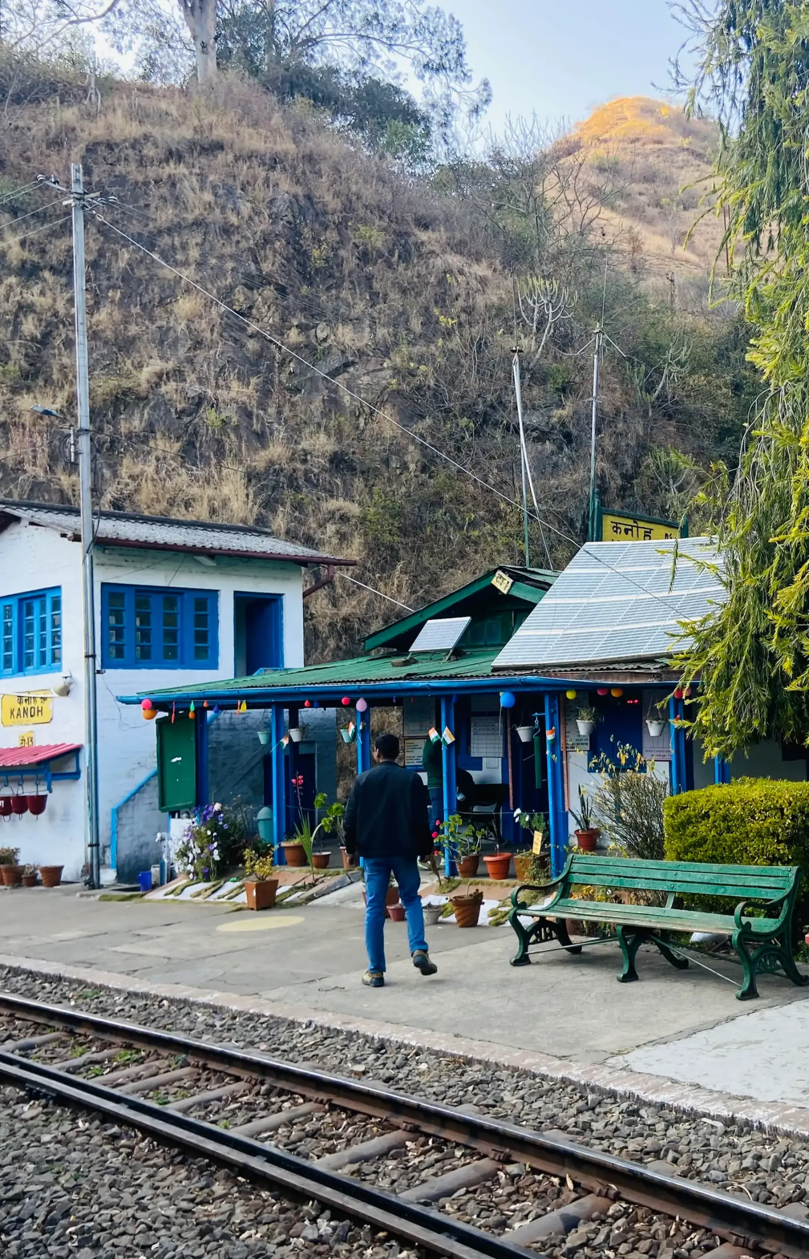 Small hill railway station with a blue and green building, a bench and the tracks in front