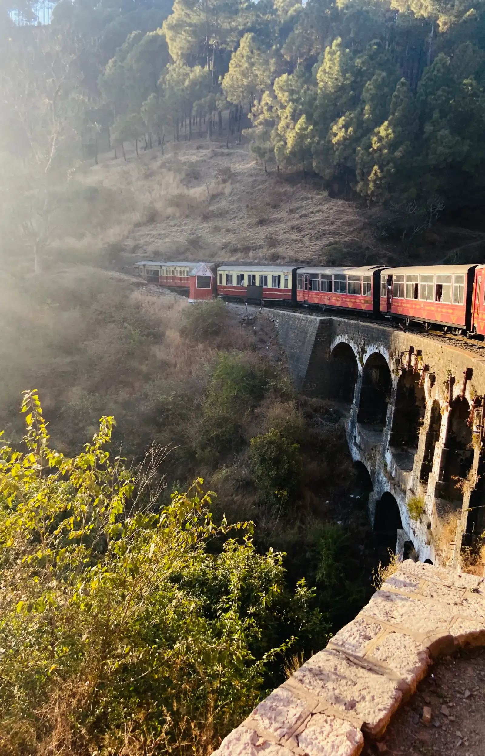 Red toy train crossing an arched stone bridge on a misty hillside