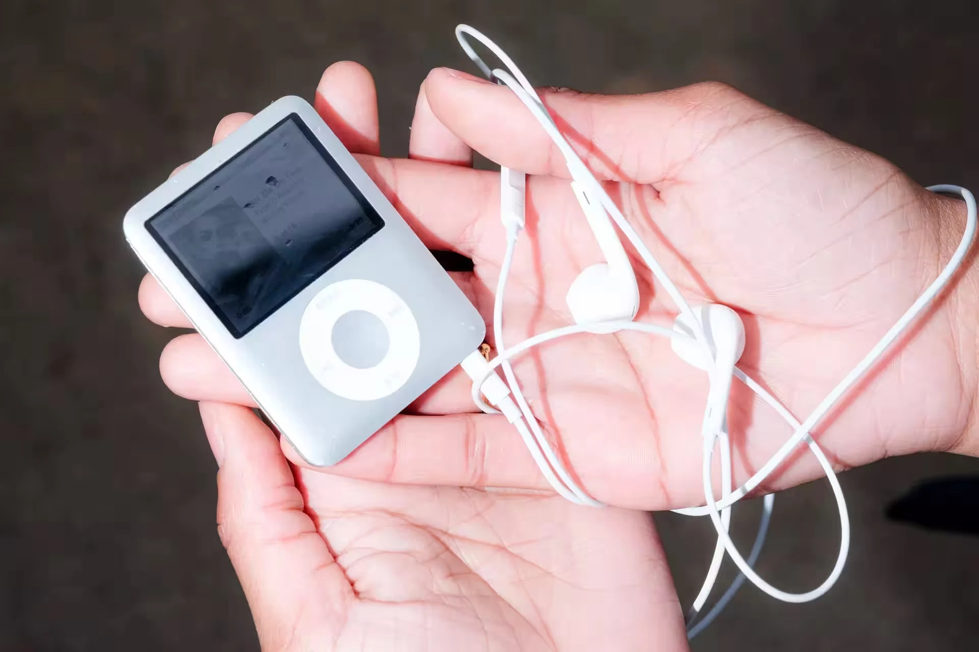 A silver iPod held in two hands with white earphones coiled around them